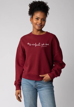 Bordeaux sweatshirt met een losse pasvorm, voorzien van witte tekst die zegt "Zo eenvoudig is dat." Lange mouwen met ribgebreide manchetten.