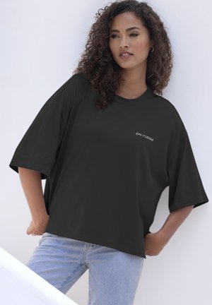 Schwarzes übergroßes T-Shirt mit kurzen Ärmeln und rundem Ausschnitt, mit weißem Logo "CPH STUDIOS" auf der linken Seite.