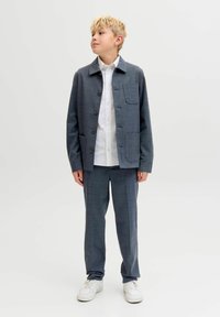 Szürke kockás zakó, gombos inggel és négy zsebbel, szürke nadrággal és fehér sportcipővel párosítva.