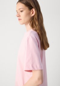 T-shirt in cotone rosa chiaro con vestibilità comoda, maniche corte e scollo rotondo, caratterizzato da una texture liscia e dettagli di cucitura minimi.