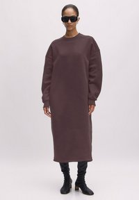Oversized bruin sweatshirt jurk met lange mouwen en een ronde hals, met een rechte snit en gecombineerd met zwarte laarzen met hakken tot de enkel.