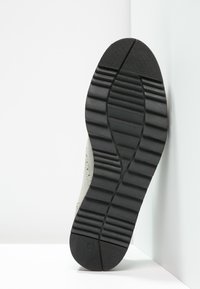 Šedá podrážka tenisky s texturovaným černým gumovým dnem; obsahuje horizontální a vertikální drážky pro trakci; viditelný jemný svrchní materiál.