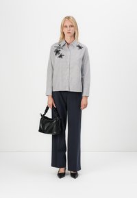 Camicia a righe con ricami floreali neri, abbinata a pantaloni ampi blu navy. Gli accessori includono una piccola borsa nera e tacchi.