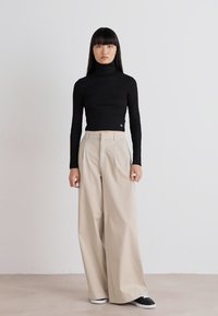 Black long-sleeve turtleneck, light beige wide-leg trousers, black sneakers. Smooth fabrics, fitted top, roomy bottoms. Minimalist style.