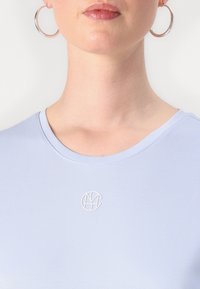 Light blue fitted t-shirt with a round neck and a subtle white logo on the chest. Smooth, stretchy fabric enhances comfort and fit.