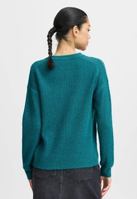 Pull en tricot c�ôtelé teal avec une coupe relaxe, un col rond et des manches longues. La texture semble douce et chaude.