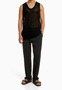 Black knit tank top with ribbed texture, paired with loose black trousers and black sandals featuring a cork sole.