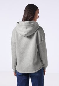 Sudadera con capucha gris de corte relajado, que presenta una gran capucha, hombros caídos y puños y dobladillo acanalados. Textura de tela suave.