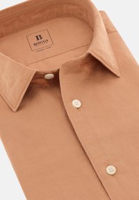 Bež srajca iz TENCEL lanenega materiala z ostrim ovratnikom, dvema belima gumboma spredaj in gladko teksturo. Neatno zložena z vidnim šivanjem.