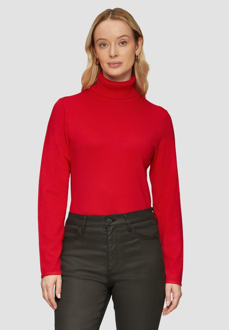 Rode coltrui gemaakt van gebreide stof met lange mouwen, gecombineerd met een donkere broek. Het ontwerp heeft een aansluitende silhouette en een gladde textuur.