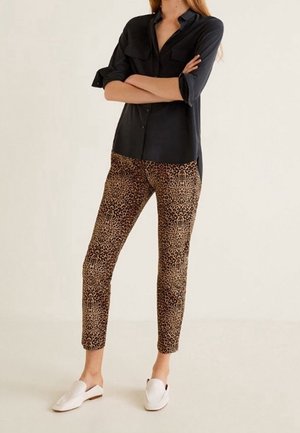 Chemise noire à manches longues avec deux poches poitrine et des poignets retroussés, assortie à un pantalon léopard ajusté et des chaussures blanches à enfiler.