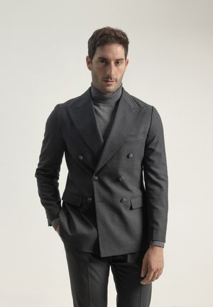 Blazer gris de lana con doble botonadura y solapas de picos, con dos grandes botones y un jersey de cuello alto ligero a juego. Corte ajustado.