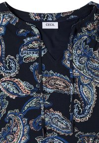 Blouse bleu foncé avec motifs cachemire multicolores, col en V avec cordons noirs, et une étiquette blanche portant la mention "CECIL" à l'encolure.