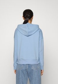 Jasnoniebieska hoodie wykonana z miękkiej bawełny, z kapturem na sznurku, prążkowanymi mankietami i krojem cropped. Połączona z jasnymi dżinsami.