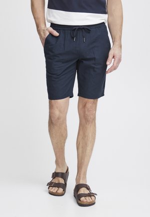 Marineblaue Leinenshorts mit elastischem Bund und Zugkordel. Verfügt über seitliche Taschen und eine lockere Passform, kombiniert mit braunen Sandalen.