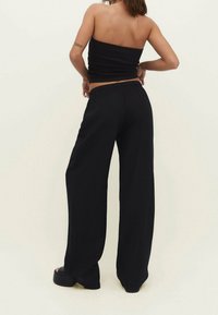 Haut noir bustier associé à un pantalon large noir et fluide. Le tissu semble léger avec une texture lisse ; détail taille élastique visible.