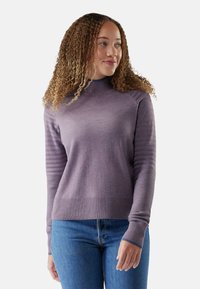 Maglione viola a maglia con un alto collo, polsini a costine e dettagli testurizzati sulle maniche. Abbinato a jeans blu.