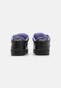 Ténis de couro preto com sola plana, apresentando um colar almofadado roxo e um logótipo em relevo no calcanhar. Acabamento texturizado com design simples.
