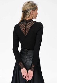 Czarna bluzka z długim rękawem, z koronkowym wzorem na plecach i koronkowymi akcentami na rękawach, w połączeniu z czarną skórzaną spódnicą o wysokim stanie z zamkiem błyskawicznym.