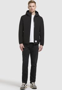 Black hooded jacket made of smooth, lightweight material, paired with a white T-shirt, dark jeans, and black-and-white sneakers.