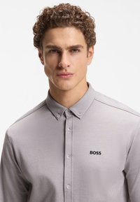 Ανοιχτό γκρι πουκάμισο με γιακά και υφή στο ύφασμα, με κουμπότρυπες και μικρό μαύρο λογότυπο "BOSS" στο αριστερό στήθος.
