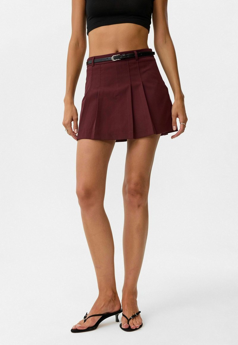 Een bordeauxrode geplooide rok met een aansluitende tailleband en een zwarte riem. Het ontwerp heeft een gladde textuur, is knieboven en heeft een uitlopende vorm.