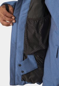 Giacca blu con un materiale esterno testurizzato, foderatura nera a contrasto e tasca interna in rete. Include chiusure a bottone sulle maniche.
