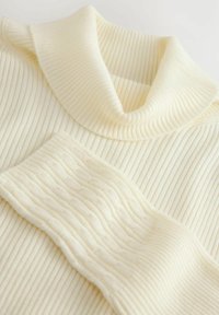 Ribbende cremefarvet sweater med høj krave, der har teksturerede vandrette og lodrette mønstre for ekstra dybde og visuel interesse.