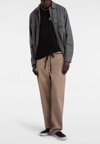 Camisa de botones gris a rayas sobre una camiseta negra, combinada con pantalones beige y zapatos negros tipo mocasín. Diseño claro con elementos prácticos.