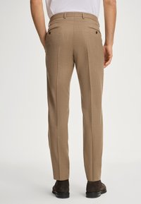Pantaloni marroni texture con una vestibilità dritta, caratterizzati da due tasche posteriori e dettagli con bottoni, indossati con calzature scure.