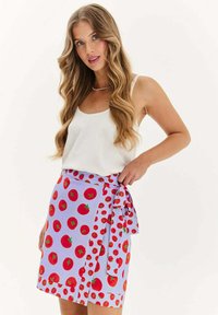 Sukňa s fialovým pozadím, na ktorom sú veľké červené vzory paradajok. Má zaviazaný pás. Hladká textúra látky.