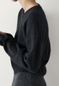 Ciemnoszary sweter z dzianiny z dekoltem w serek i luźnym krojem, z prążkowanymi mankietami i dolnym wykończeniem, zestawiony z pasującą szarością odzieżą.