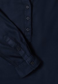 Camicia blu navy con bottoni, dalla texture morbida, sei bottoni neri lungo la patta e polsini piegati.