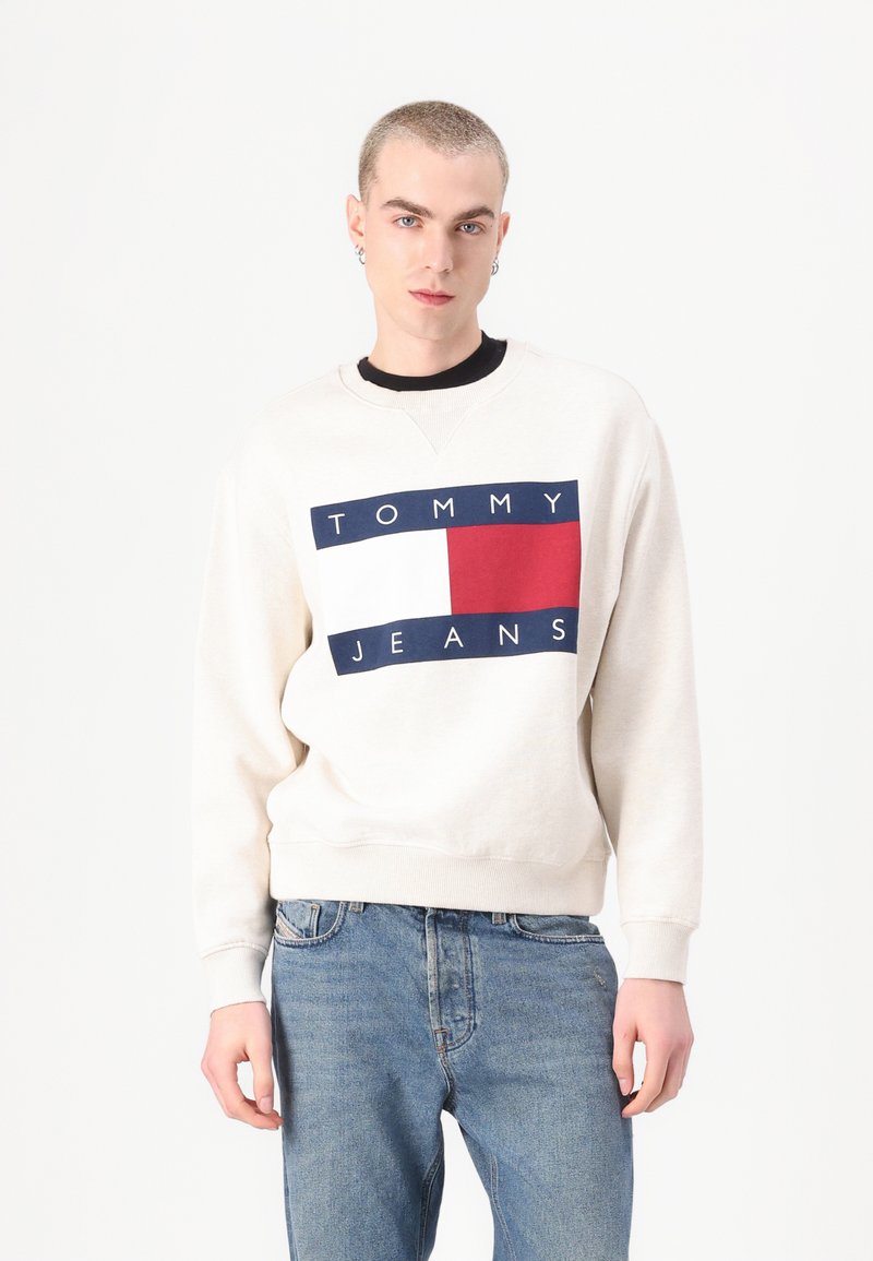 Krémová mikina s grafikou „TOMMY JEANS“ v námorníckej modrej a červenej s obdlžníkovými akcentami. V kombinácii so svetlomodrými denimovými džínami.