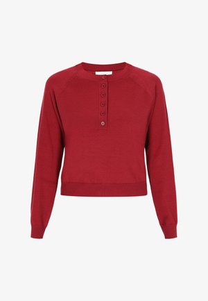 Punainen lyhyt neulepaita, jossa on pyöreä kaula-aukko, viiden napin lista ja pitkät raglan-hihat. Pehmeä neulemateriaali, jossa on ribbireunat hihansuissa ja helmassa.