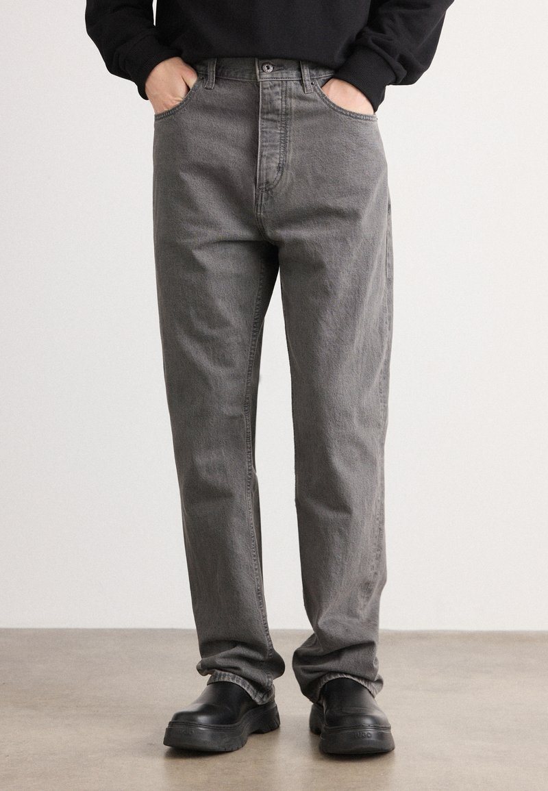 Gray denim jeans with a straight-leg fit, five-pocket design, and visible stitching. Worn with black slip-on shoes.