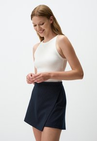 Top a righe bianco con scollo alto abbinato a una mini gonna avvolgente a righe blu navy, caratterizzata da una sovrapposizione laterale e un tessuto testurizzato.