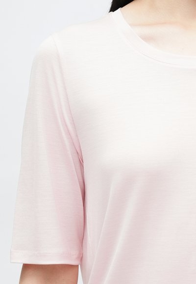 Camiseta rosa-claro de manga curta com gola redonda, fabricada em um tecido suave e texturizado. Detalhes de costura nos ombros e nas mangas.