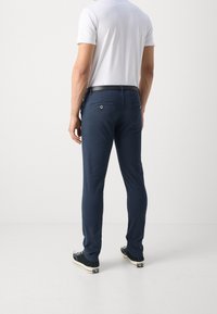 Námořnické kalhoty z bavlněné směsi, úzký střih, se dvěma zadními kapsami na knoflíky, nošené s bílým tričkem a černými teniskami.