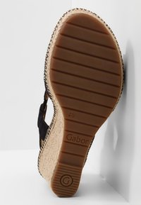Sandale compensée noire avec une semelle style espadrille texturée, dotée d'une semelle inférieure en caoutchouc marron et d'un motif de bande de roulement prononcé.