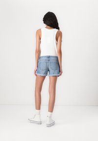Vit ärmlös topp med ögla-detaljer, kombinerad med ljusblå denimshorts. Modellen bär vita högsta sneakers med vita ankelsockor.