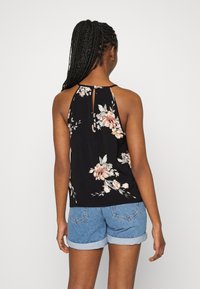 Débardeur noir à motif floral avec un col haut et un détail ajouré dans le dos, présentant des fleurs roses et blanches, accompagné d'un short en denim.