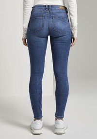Jeans ajustados azul claro con una textura suave, de cintura alta, cinco bolsillos y sutiles detalles de costura. Combinados con zapatillas blancas.