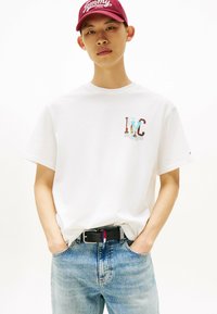 Witte katoenen T-shirt met een kleurraf "NYC" grafiek. Gekleed met lichtblauwe denim jeans en een zwarte riem met rode, witte en blauwe accenten.
