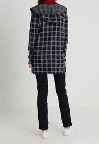 Marinblandad och grå rutad kappa med huva, långa ärmar och rak skärning, kombinerad med svarta byxor och vita sneakers.