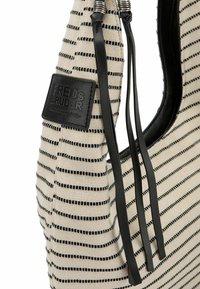 Sac à épaule en tissu rayé crème et noir, avec une étiquette en cuir, des fines anses noires et une forme arrondie. Matériau en tricot texturé.