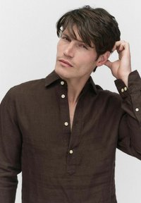 Chemise en lin marron foncé avec une patte de boutonnage, des manches longues et un col. Présente des boutons de couleur claire et une coupe décontractée.