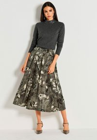 Grijze trui met een hoge hals, gecombineerd met een bloemenprint, geplooide maxi rok in donkergroen, zwart en wit. Puntige hakken.