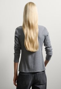 Graues, geripptes Langarmoberteil mit lockerer Passform, kombiniert mit dunkelblauem Jeansstoff, von hinten vor einem schlichten Hintergrund betrachtet.