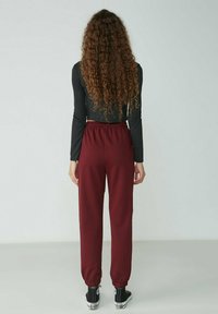 Burgunderfarbene Jogginghose mit elastischem Bund und Bündchen, aus glattem Stoff, kombiniert mit einem eng anliegenden schwarzen Langarmoberteil.